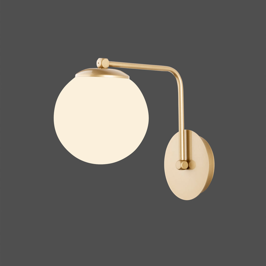 Applique murale à bras doré avec globe blanc opale allumé sur fond sombre
