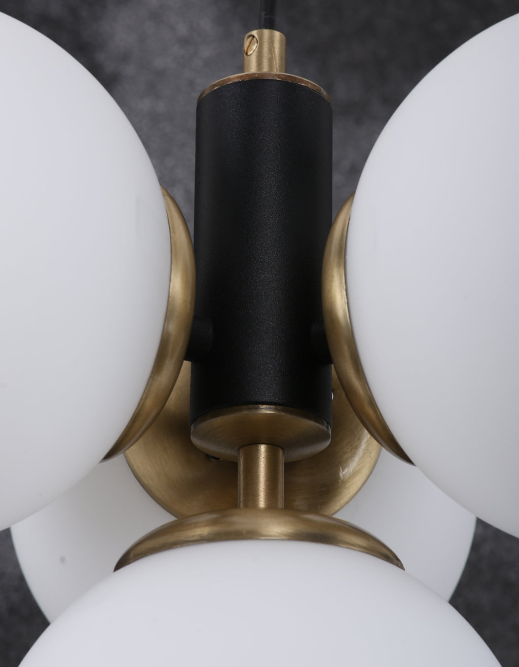 Détail de la structure noir mat avec finition laiton entre les globes en verre blanc opale