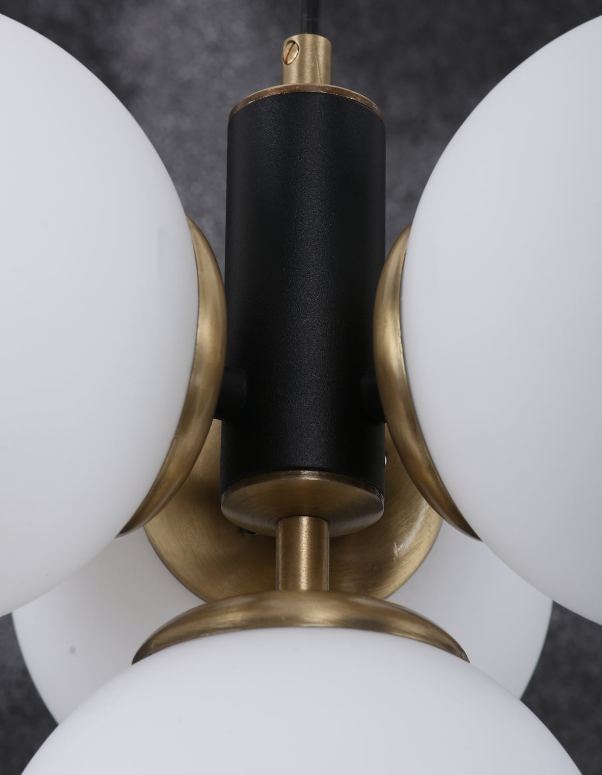 Détail de la structure noir mat avec finition laiton entre les globes en verre blanc opale