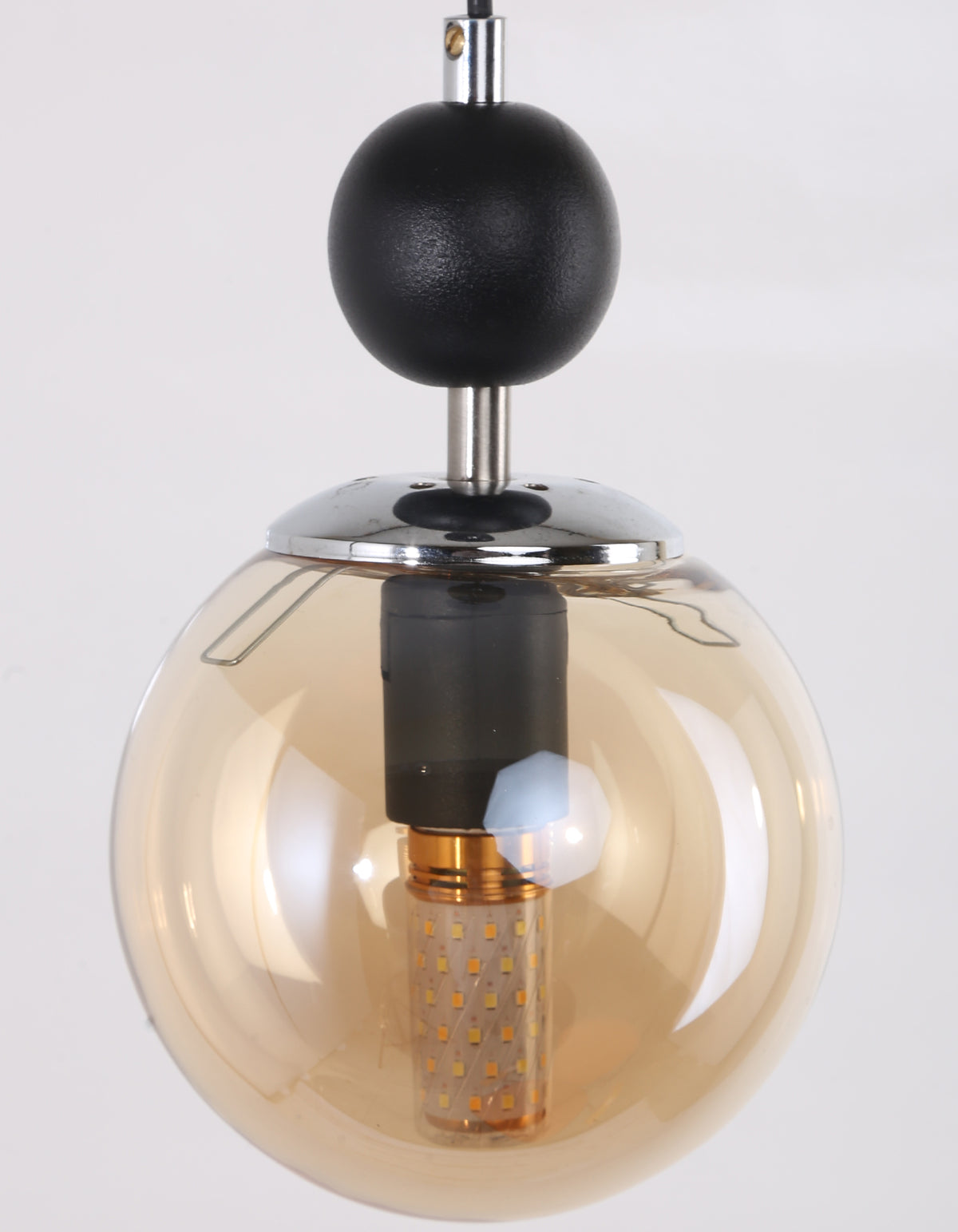 Gros plan du globe en verre ambré et de la monture chromée du lustre suspendu