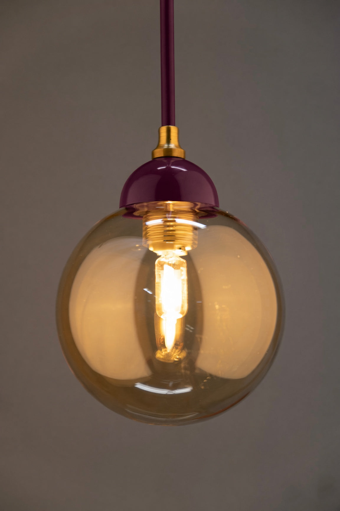 Détail du globe en verre ambré et de la finition bordeaux et dorée de la suspension