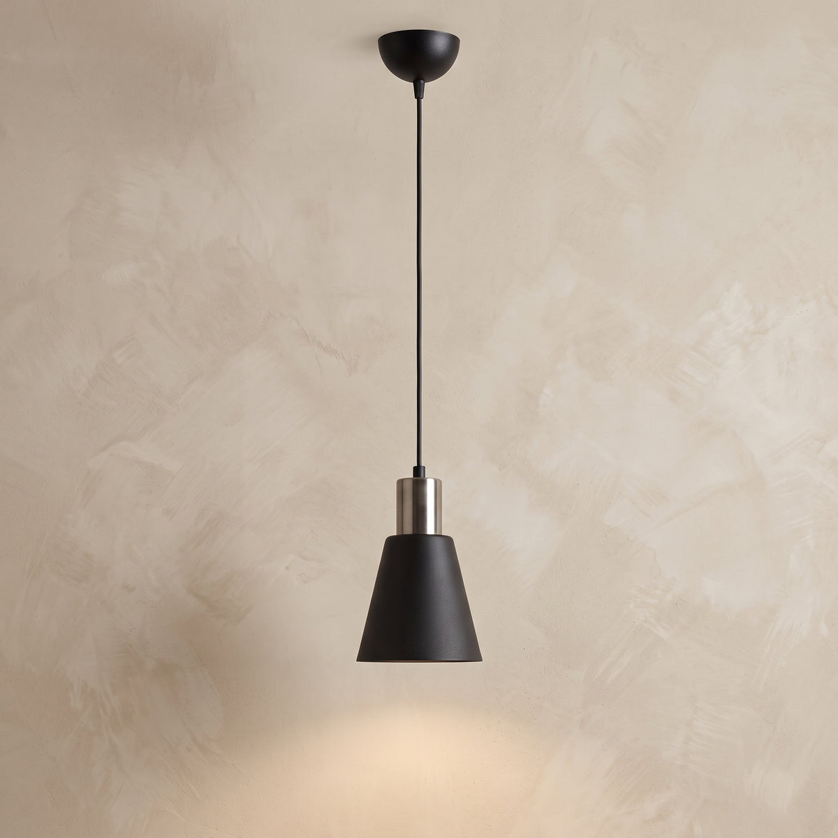 Suspension conique noir mat et détails argentés de 14 cm de diamètre sur fond beige texturé