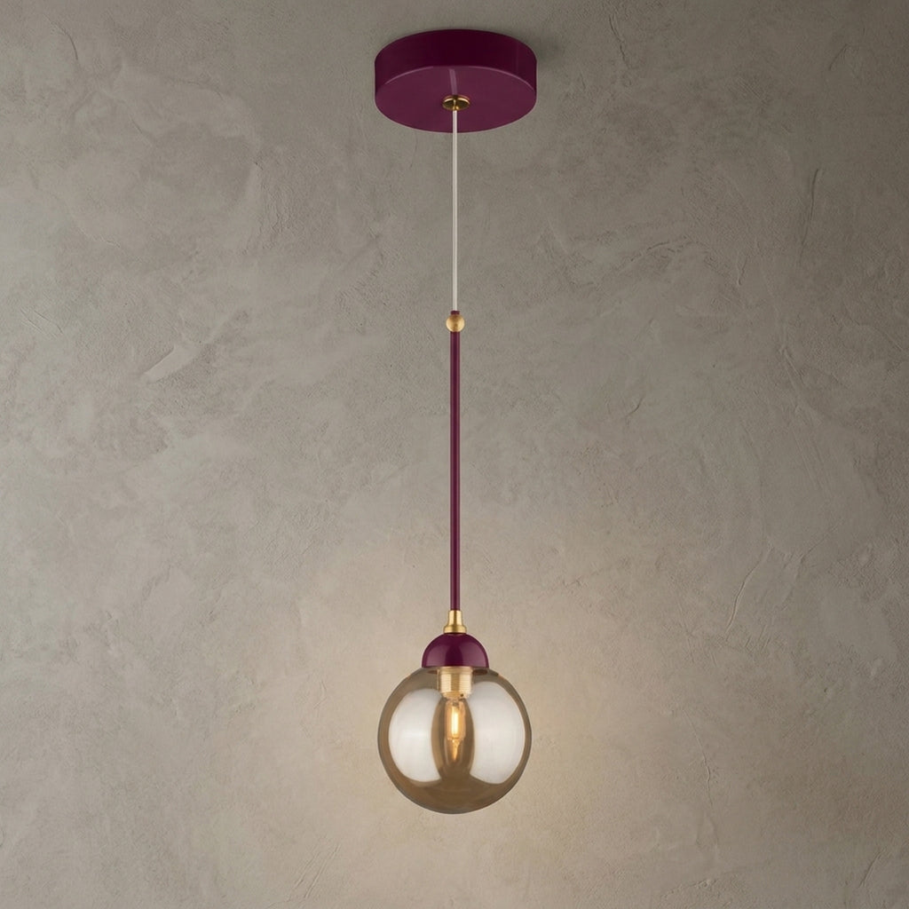 Suspension bordeaux avec détails dorés et globe rond en verre ambré allumé sur fond beige