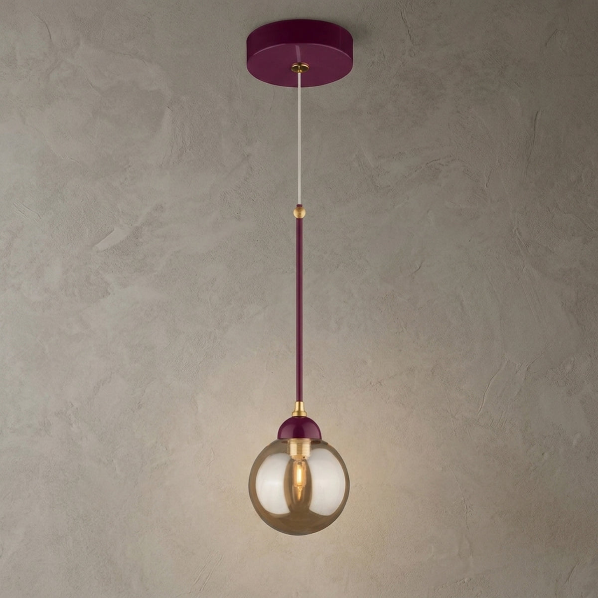 Suspension bordeaux avec détails dorés et globe rond en verre ambré allumé sur fond beige